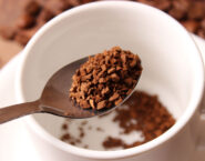 spoon with instant coffee granules over white mug