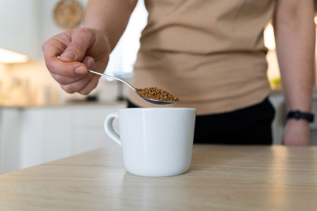 man holding spoonful of instant coffee over mug